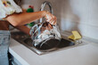 © qunica.com - A woman is washing a metal pot with soapy water in a kitchen sink. The image captures a daily chore, emphasizing cleanliness and routine in a domestic setting.