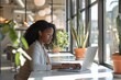 © Odin AI - In a modern cafe filled with natural light and greenery, a focused woman wearing headphones uses a laptop, symbolizing the blend of technology and relaxation in today's lifestyle.