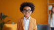 © NaphakStudio - cheerful young boy with curly hair wearing glasses and stylish orange suit stands confidently against vibrant yellow background, exuding charm and positivity.