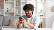 © YURII MASLAK - Satisfied Indian man checking his email and happy with good news. A young man winner celebrating the victory sitting at the table, raises his hands uphill.