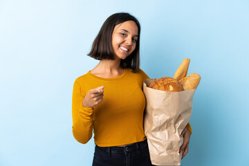 Young latin woman buying some breads isolated on blue background pointing front with happy expression