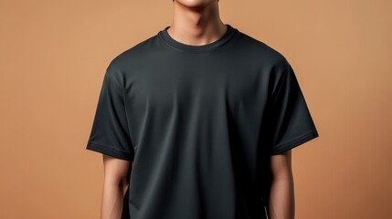 A young man wearing a dark t-shirt against a warm, muted background, showcasing contemporary casual fashion.