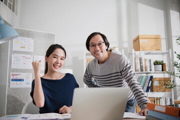 Two young Asian startup company entrepreneur partners brainstorm in casual small business office, marketing planning jobs on laptop, freelance work as E-commerce, happy and cheerful coworker team.