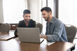 © fizkes - Two positive young male Middle Eastern entrepreneurs working on Internet project, online startup together, watching website media content, pointing at monitor, smiling, sitting at table together