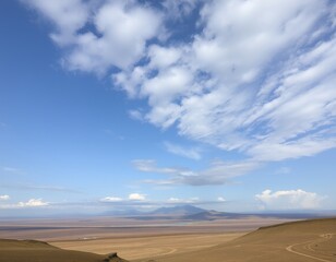 A vast, open landscape with a mountain range in the distance, under a sky filled with fluffy clouds.