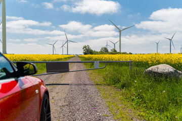 Wind generators in rapeseed field and car in front of security barrier. Blocked road. Alternative energy.