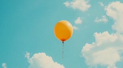 A single yellow balloon floats against a bright blue sky with white clouds.