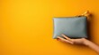 © Maximages  - A simple yet striking image of a hand holding a sleek blue pouch against a vibrant orange background, combining minimalist style with bright and bold color contrasts.