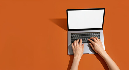 Two hands typing on laptop with blank screen orange surface