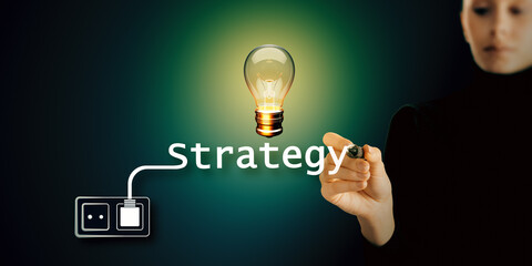 Person writing Strategy with connected lightbulb visual on dark background. Concept of business ideas and innovation.