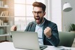 © useful pictures - Overjoyed millennial man celebrating a victory while working from his bright home office in the morning