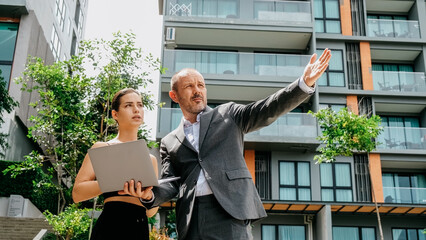 A businessman and a young female assistant discuss a new project outdoors while using a laptop. Their collaboration highlights a dynamic and modern approach to work.