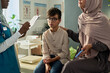 © pressmaster - Young boy sitting on examination table while Muslim doctor taking notes and parent looking attentively at doctor in a clinic setting
