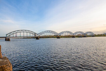 Wall Mural - A modern electric passenger train crosses the railway bridge (Dzelzcea tilts) over the Daugava River. Taking passengers to the scenic Jurmala region of Latvia.