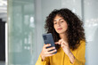 © Liubomir - Latin American businesswoman with curly hair using phone in office. She wears yellow clothing, showing focus and determination. Concept of innovation, technology, and professional confidence.