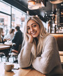 © Hoss - Photo portrait of a beautiful woman at a cafe, bar or restaurant smiling with a sensual look, she wears a cozy fall sweater, her hand on her cheek as she looks at the camera.
