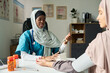 © pressmaster - Muslim female doctor wearing a hijab checking a patient blood pressure in a modern clinic setting with medical posters and equipment visible in the background