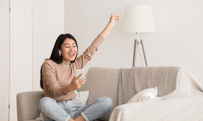 Wall Mural - Happy Girl Enjoying Music In Airpods And Singing Favourite Song, Relaxing On Sofa