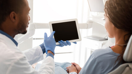 Dentist black guy pointing at blank digital tablet screen, doctor showing female patient new application, close up