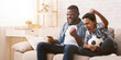 © Prostock-studio - Afro father and son soccer fans watching football on tv at home and emotionaly cheering, sitting with soccer ball on couch in living room