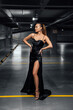 © Alex - Stylish sexy girl in a black dress with a cutout in the parking lot near an expensive stylish car