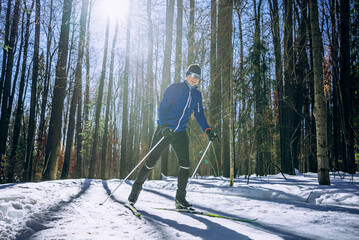 Man enjoys cross-country skiing in a snowy forest, with the sun shining through the trees, creating a warm atmosphere