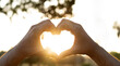 © busra - Hands in shape of love heart at sunset. The sun is setting in the background, creating a warm and romantic atmosphere.