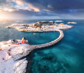 aerial view of road and bridges, snowy islands with red rorbu, sea, water, mountains, cloudy sky at 