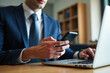 © Minerva Studio - Businessman using smartphone and typing on laptop at work
