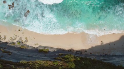 Wall Mural - Clear blue ocean waves gently lap against a sandy beach with two small rocky islets in the distance under a bright sky.