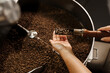 © Rabizo Anatolii - Handful of fried coffee grains. Roasted coffee beans in roasting machine in the production. High quality coffee beans manufacturing.