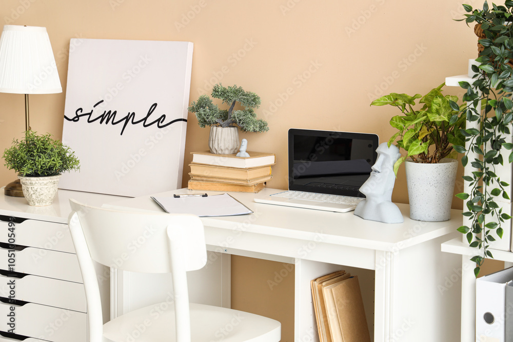 Blank laptop with books and plants on table in office