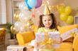 © Pixel-Shot - Cute little girl in party hat with balloons, gifts and decorations for birthday at home