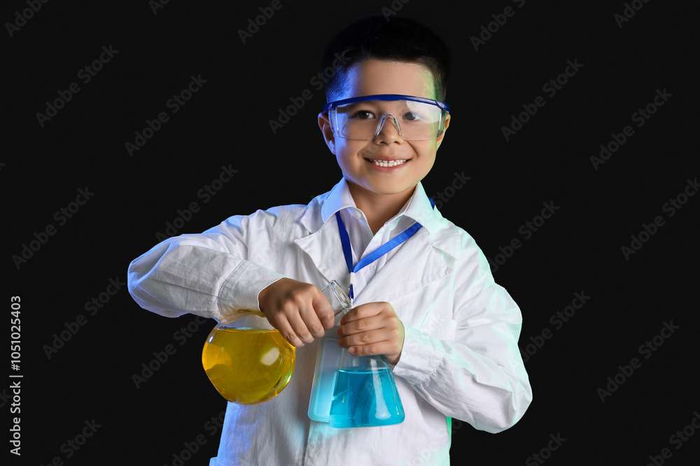 Cute little boy conducting experiment with chemical flasks on black background