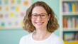© tashechka - A confident teacher stands in a colorful classroom, smiling warmly while holding a book, ready to inspire her students