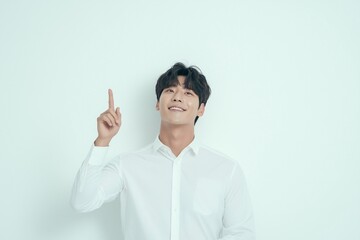 Happy young Korean businessman or college student standing isolated on a simple background presenting promotion ads. Smiling man looking upward pointing up at copy space, having new idea.