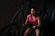 © kamonrat - Determined Woman Exercising with Battle Ropes in a Dark Gym, Demonstrating Strength, Endurance, and Fitness Motivation