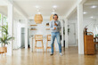 © eggeeggjiew - Middle aged man enjoying music and dancing in a modern kitchen, wearing headphones and holding a smartphone, expressing joy and relaxation.