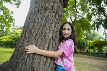 cute young indian girl child embracing large tree. Save planet, ecology, climate change, nature lover,