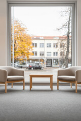 Cozy seating area with two armchairs and a table overlooking a vibrant city street in autumn