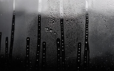 Poster - A black and white photograph of water droplets on a window pane. The droplets are clustered together in vertical lines, giving the illusion of raindrops running down the glass.