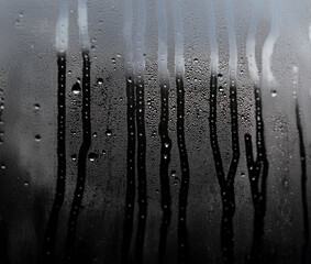 Poster - Condensation streaks and droplets form on a cool window pane, blurring the view of the outside.
