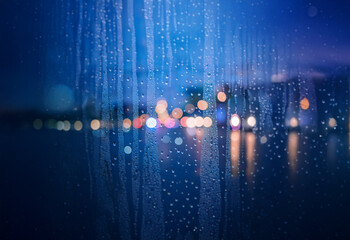Aufkleber - A blurry cityscape with a dark blue sky seen through rain-streaked glass.