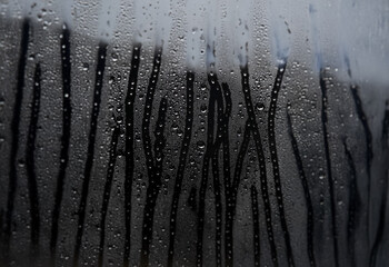 Poster - Raindrops gather on a window pane, obscuring the view beyond with a misty film.
