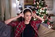 © Halfpoint - Student having hygge Christmas at home. Woman is sitting on sofa by Christmas tree, listening music with headphones.