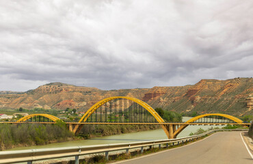 A yellow bridge spans a river in a mountainous area