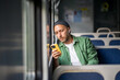 © DimaBerlin - Thoughtful man concentrating on mobile phone rides on electric train reading e-book, scrolling social media, listens to music on headphones to pass time, leaning to window. Public transport trip alone