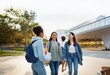 © YiuCheung - Three students are walking in front of a modern building, they are smiling and talking to each other.