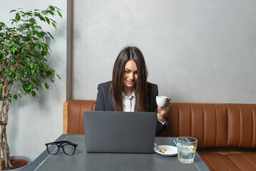 One young businesswoman sitting in cafeteria taking a coffee break while working online on laptop computer. Business female professional occupation e-commerce and remotely finance and economy research