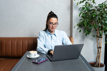 One young businesswoman sitting in cafeteria taking a coffee break while working online on laptop computer. Business female professional occupation e-commerce and remotely finance and economy research